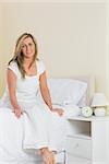 Pleased mature blonde woman looking at camera and sitting on a bed in a bedroom