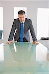 Serious mature businessman standing firmly in front of a desk at office