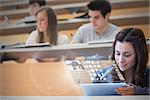 Focused pretty student working on her futuristic tablet in lecture hall