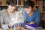 Students using futuristic hologram to learn biology from tablet sitting in college library