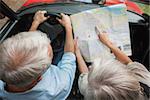 Overhead view of mature couple on holidays reading map in their classy convertible