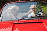 Cheerful mature couple in red cabriolet going for a ride on sunny day