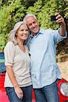 Smiling mature couple taking pictures of themselves leaning against their cabriolet