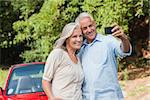 Cheerful mature couple taking pictures of themselves leaning against their cabriolet