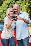 Smiling mature couple looking at pictures on their camera while leaning against their cabriolet
