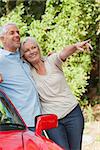 Mature couple leaning against their red cabriolet on a sunny day
