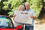 Smiling mature couple reading map by their cabriolet