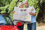 Smiling mature couple by their cabriolet reading map looking for direction