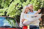Cheerful mature couple by their cabriolet reading map looking for direction
