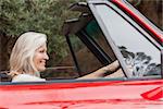 Happy mature woman driving red convertible on sunny day