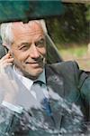 Cheerful businessman on the phone driving expensive car