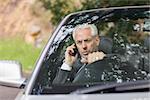 Content businessman on the phone driving expensive cabriolet on sunny day