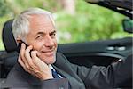 Cheerful businessman on the phone driving expensive cabriolet on sunny day