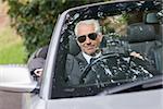 Cheerful mature businessman driving classy cabriolet on sunny day