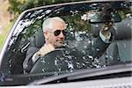 Mature businessman adjusting his cabriolet rear view mirror while driving