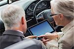 Mature partners working together on tablet in classy convertible on a bright day
