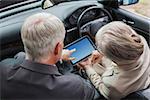 Mature partners working together on tablet in classy car on a bright day