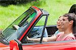 Smiling young couple having a ride in red cabriolet on a sunny day