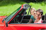 Cheerful young couple having a ride in red cabriolet on a sunny day