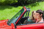 Pretty blonde kissing her boyfriend in red cabriolet on a sunny day