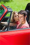 Happy blonde kissing her boyfriend in red cabriolet on a sunny day
