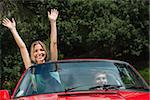 Happy woman having fun in red classy cabriolet while her boyfriend driving