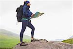 Woman standing on a rock holding map on a hike in the countryside