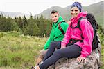 Couple sitting on a rock resting during hike smiling at camera