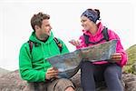 Couple using map and compass sitting on a rock during their hike