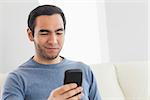 Smiling casual man text messaging in cosy bright living room