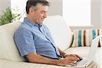 Smiling mature man sitting on a sofa typing on a laptop in a living room