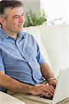 Thinking mature man sitting on a sofa in a living room using a laptop