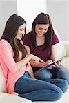 Two smiling teenage girls sitting on a sofa using a tablet pc in a living room