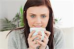 Smiling brunette drinking a cup of coffee at home looking at camera