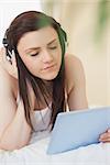 Relaxed girl listening to music with a headset and using a tablet pc lying on a bed in a bedroom