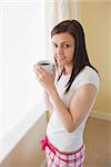 Smiling brunette looking at camera and drinking a cup of coffee in a bedroom