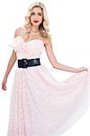 Stylish blonde model in pink dress posing holding her dress on white background