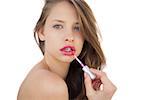 Focused brunette model applying gloss on her lips on white background