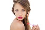 Thoughtful brunette model applying gloss on her lips on white background