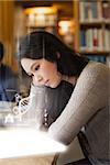 Student using futuristic hologram to learn about dna from tablet sitting at desk in library