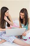 Cheerful friends in pajamas talking on bed using a laptop at home in bedroom