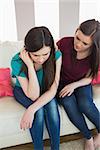 Girl comforting her upset crying friend on the couch at home in living room