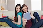 Girl showing her friend her tablet pc on the sofa at home in living room