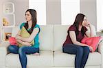 Two friends not talking to each other after fight on the sofa in sitting room at home
