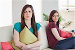 Two upset friends not talking to each other after fight on the sofa in sitting room at home