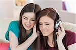 Cheerful girl listening to music with her friend beside her on the sofa in sitting room at home