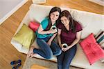 Two happy friends drinking coffee and looking at camera on the couch at home in the living room