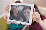 Two happy friends on the couch taking a selfie with tablet pc at home in the living room