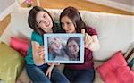 Two smiling friends on the couch taking a selfie with tablet pc at home in the living room