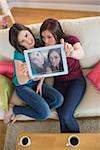 Two pretty friends on the couch taking a selfie with tablet pc at home in the living room